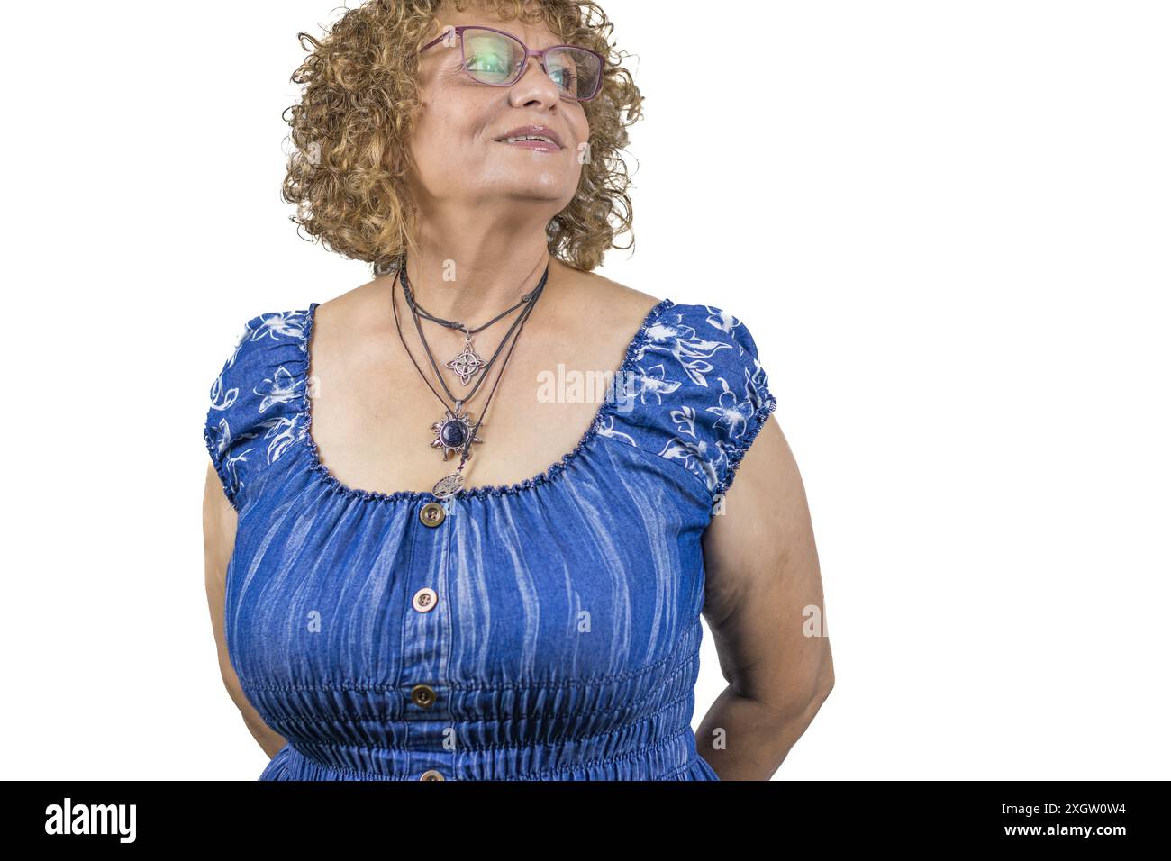 The image showcases a sixty-year-old woman standing against a white background. She is dressed in a blue, ruched blouse Stock Photo