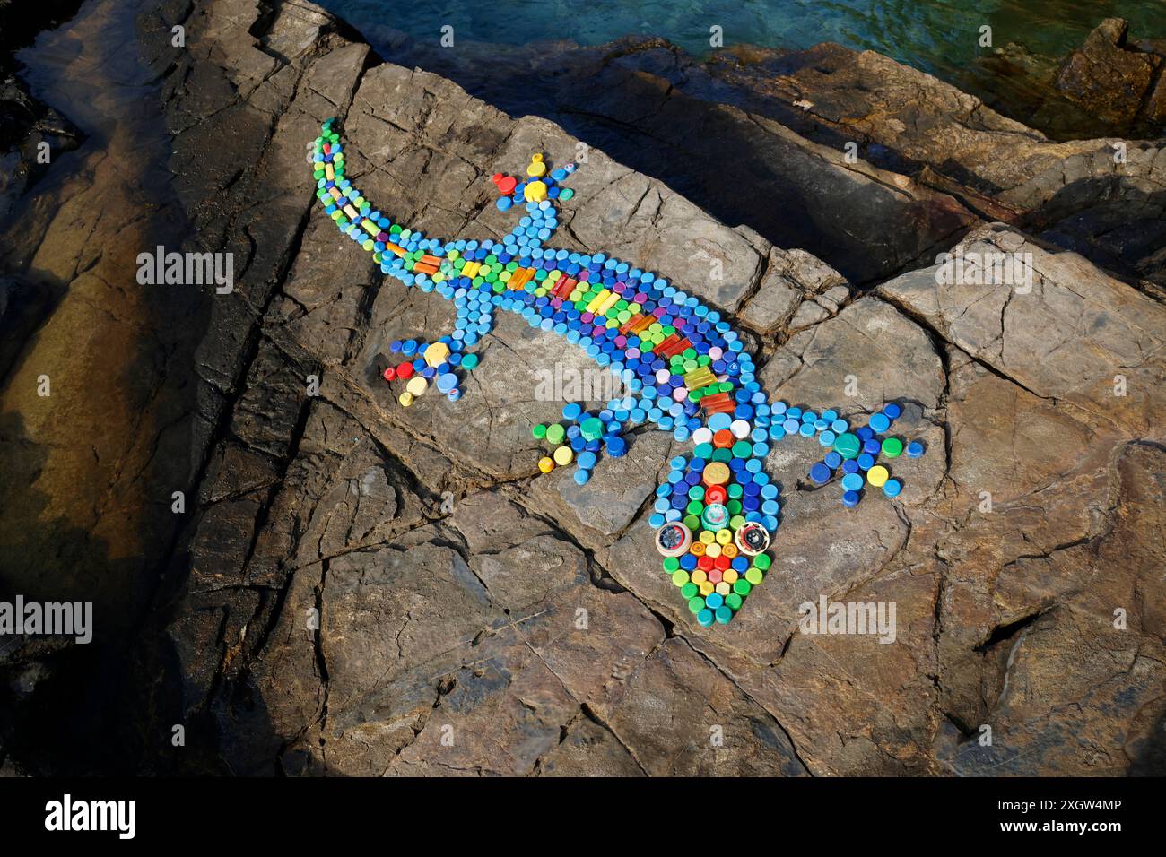 Gecko design on coastal rocks made from bottle tops and cigarette lighters collected from beaches, Milina, South Pelion, Greece Stock Photo