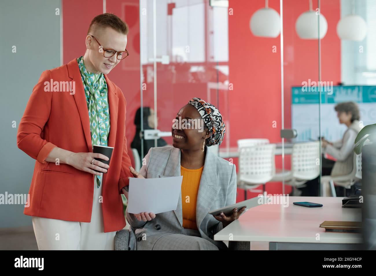 Caucasian female and African American female colleagues discussing work ...