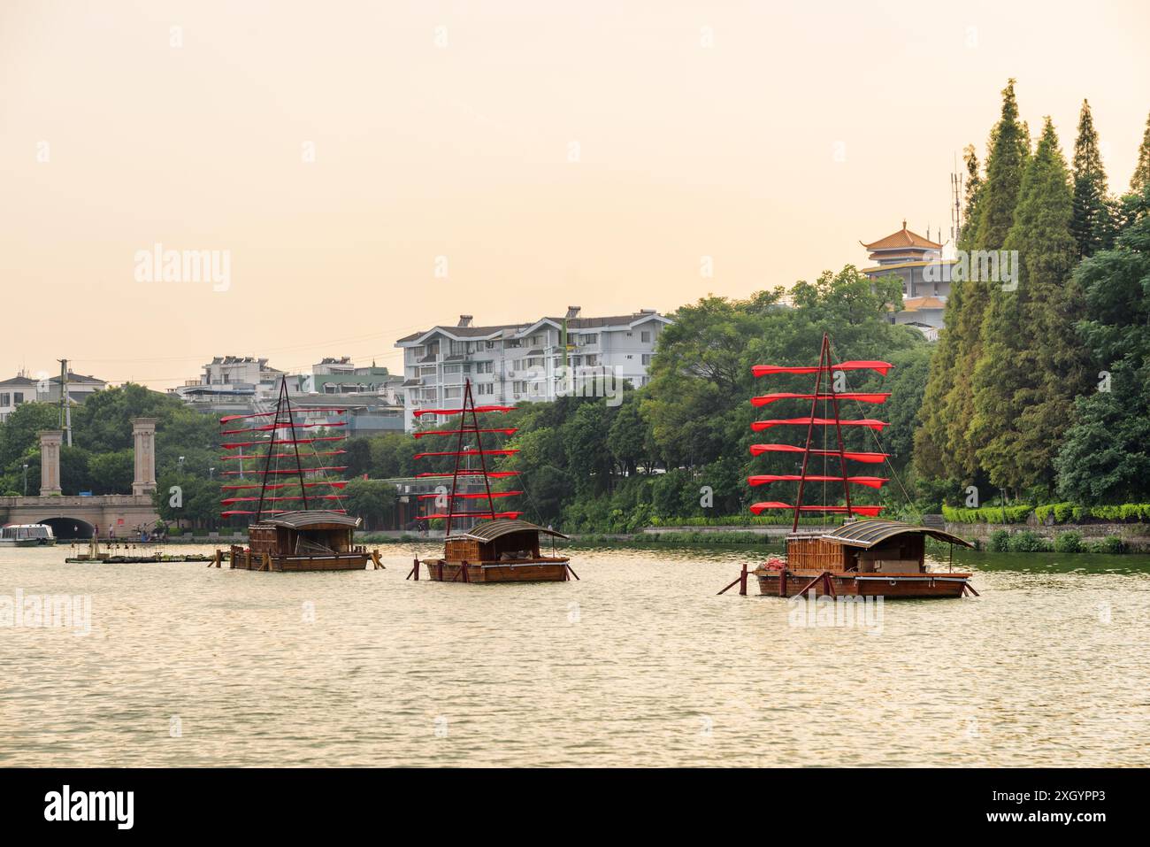 Scenic wooden ships decorated with red flags and parked on lake in Guilin, China. Beautiful view at sunset. Stock Photo