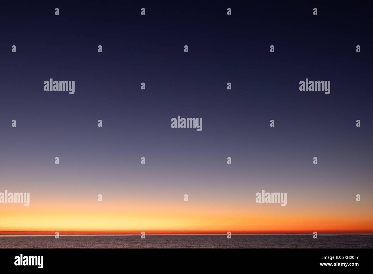 The calm waters of Canet Beach reflect the first light of dawn, creating a mirror-like effect. The serene landscape is enhanced by the soft colors Stock Photo