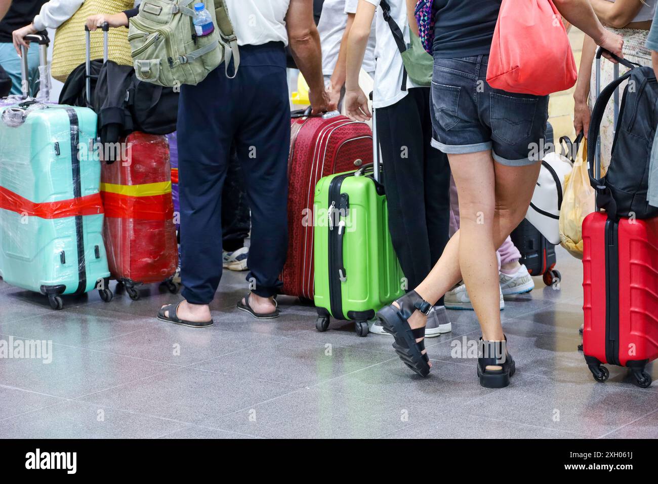 People with luggage standing in a line at airport. Suitcases on wheels on the floor, summer travel and holidays Stock Photo