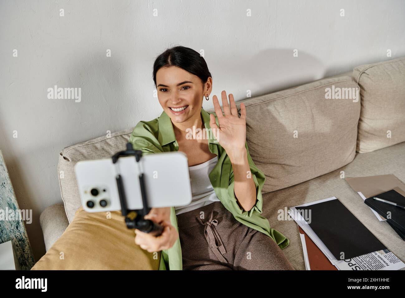 A woman in casual attire sitting on a couch, holding a phone Stock ...