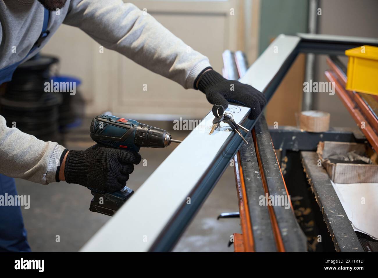 Worker in protective gloves uses drill while working with window profile Stock Photo