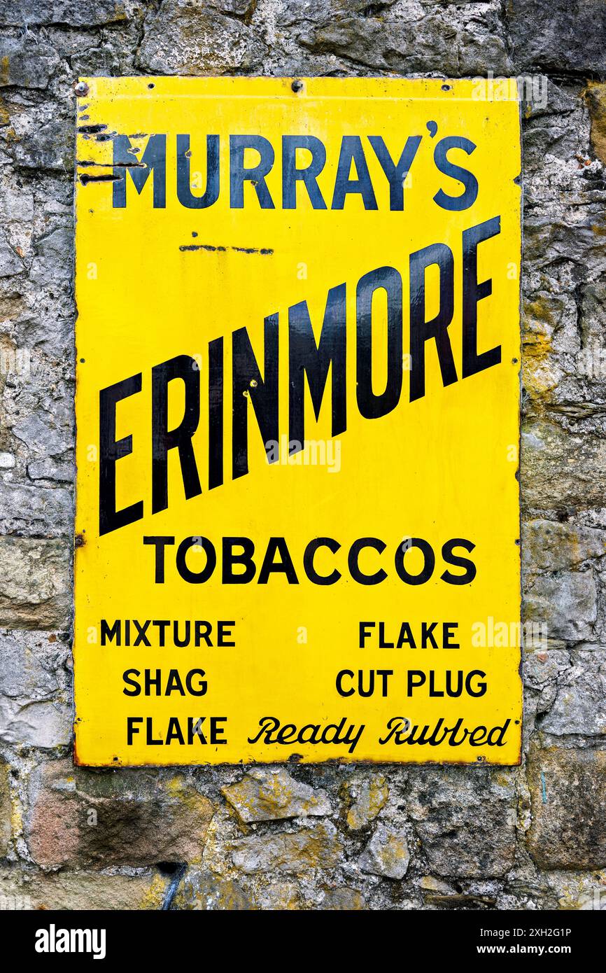 Vintage yellow tobacco advertisement sign on a weathered stone wall, highlighting various tobacco products. Stock Photo