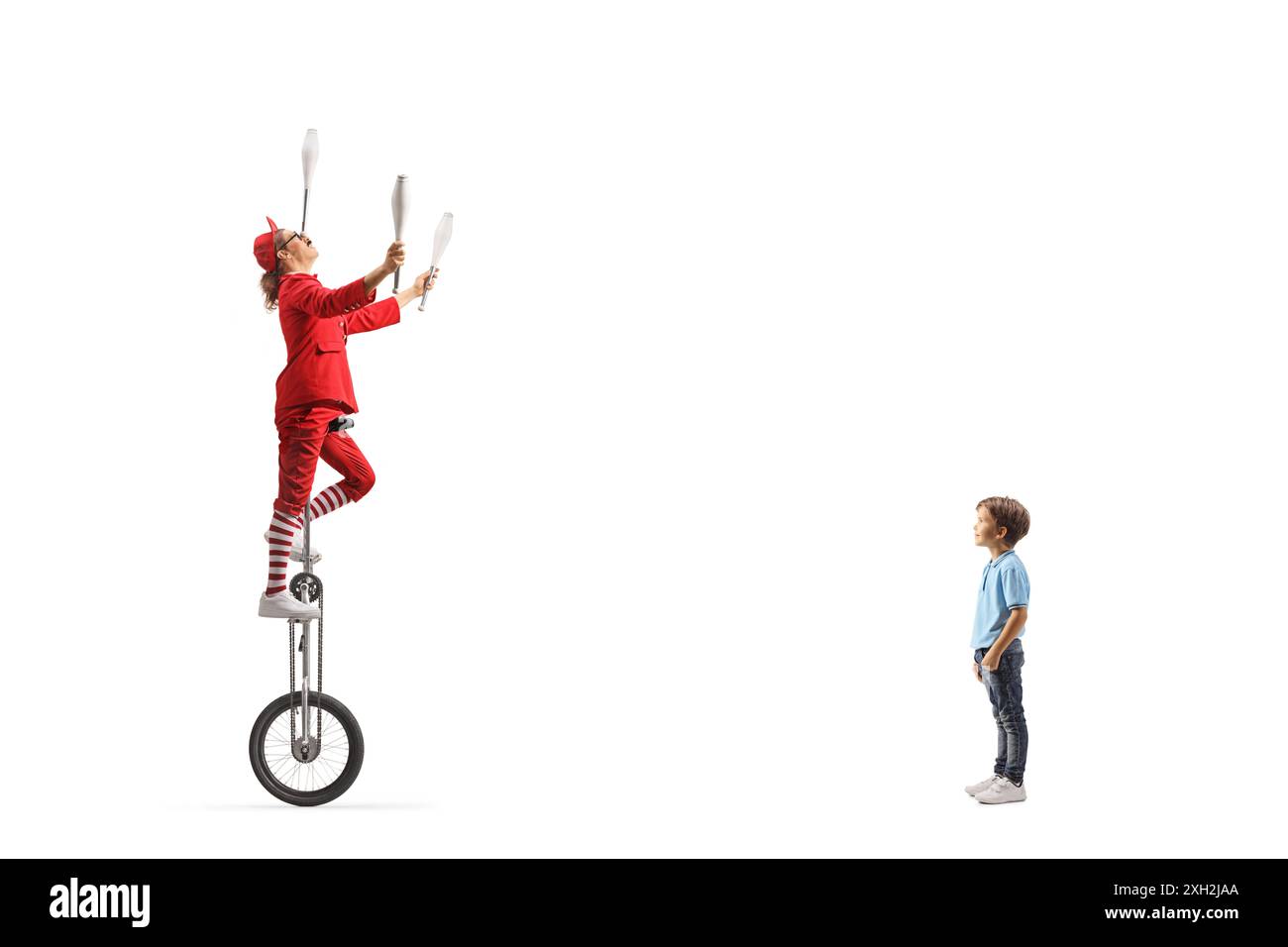 Boy watching an acrobat riding a giraffe unicycle and juggling isolated on white background Stock Photo