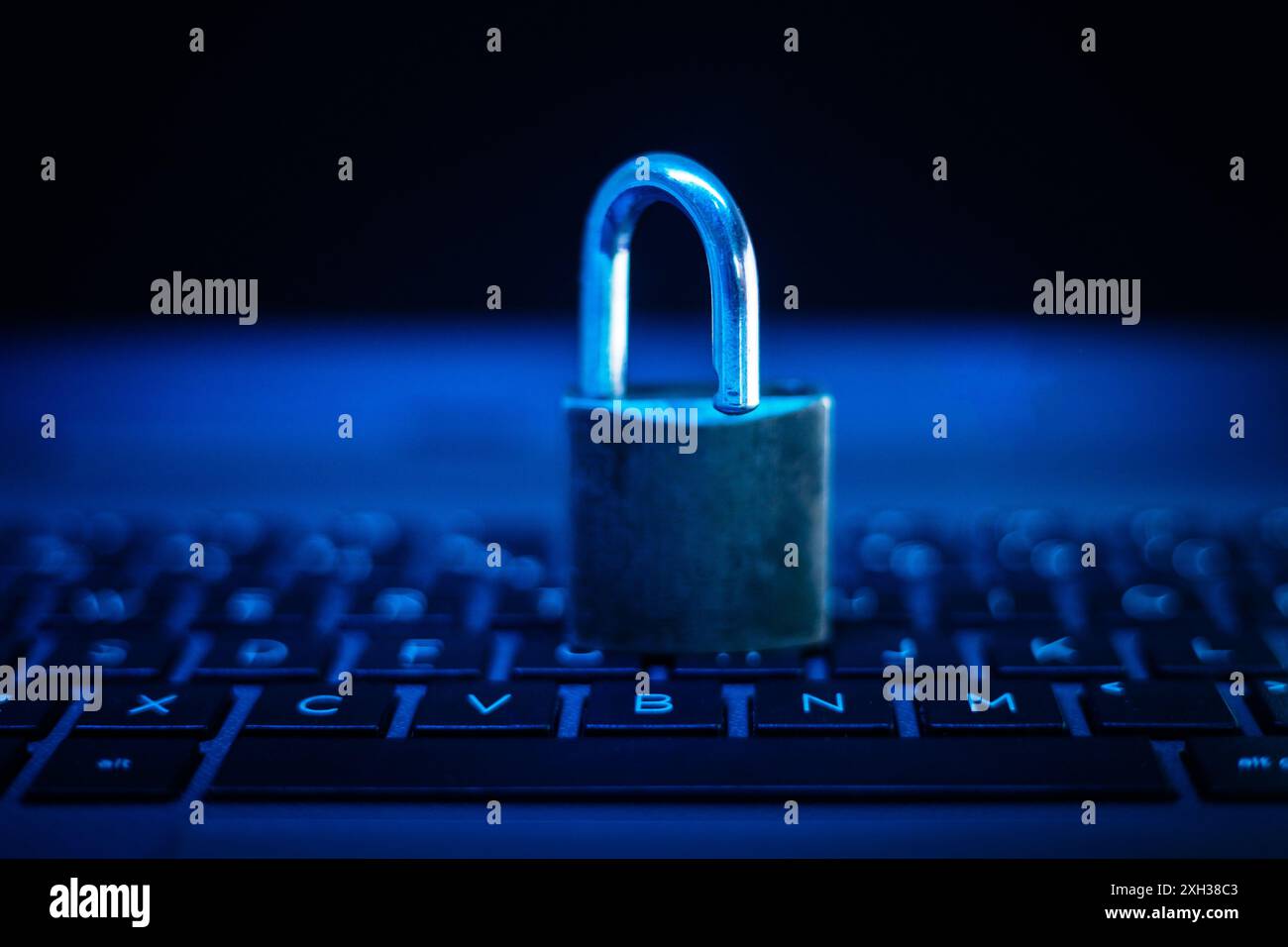 A closed padlock sits on the keys of a laptop keyboard with the room lit in a blue hue. Stock Photo