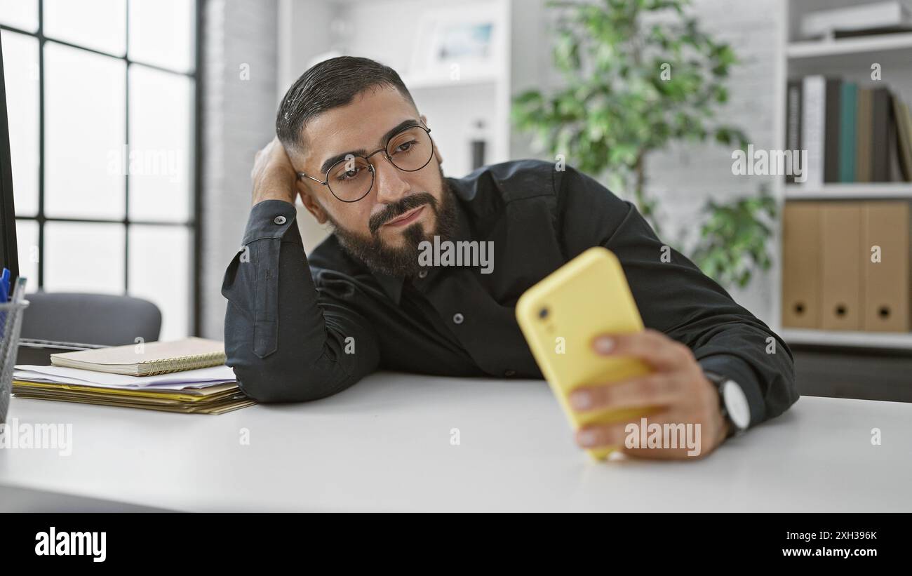 Handsome arab man in glasses using smartphone at office desk Stock Photo