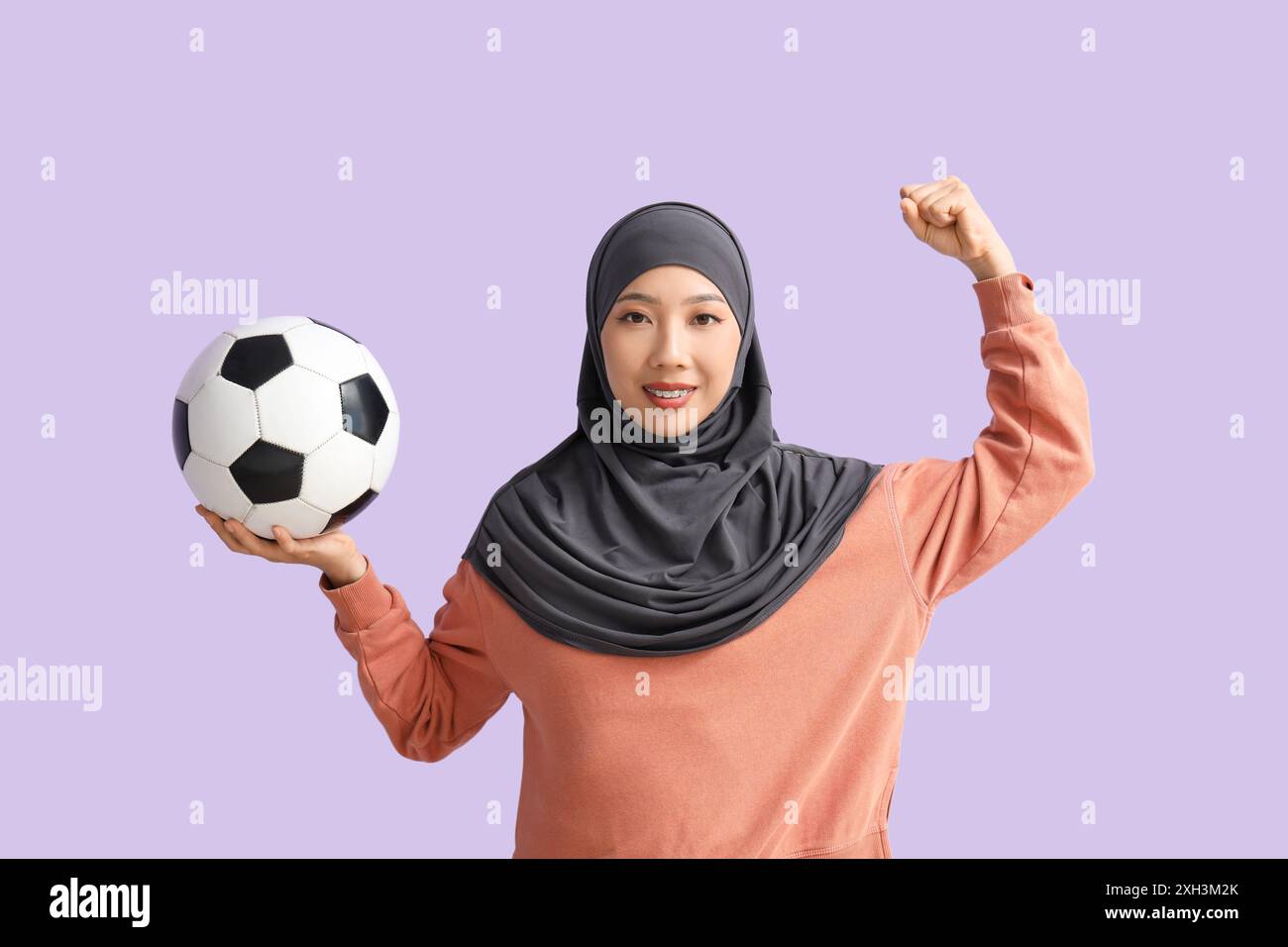 Young sporty Asian woman in hijab with soccer ball on purple background Stock Photo