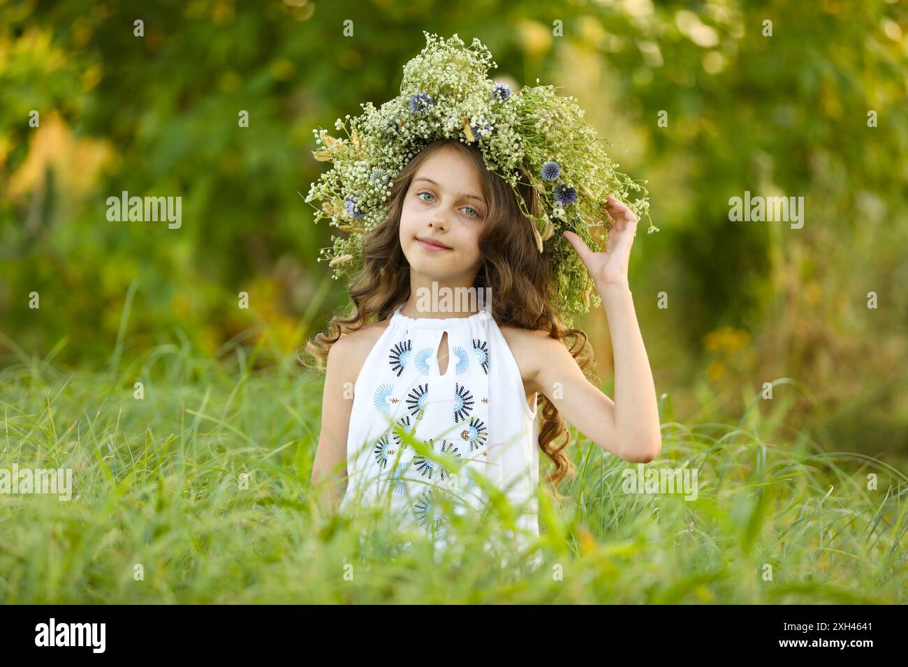 Cute little girl wearing wreath made of beautiful flowers in field ...
