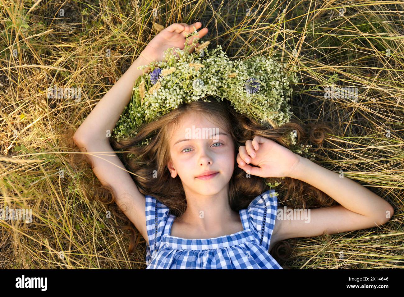 Cute little girl wearing wreath made of beautiful flowers on green ...