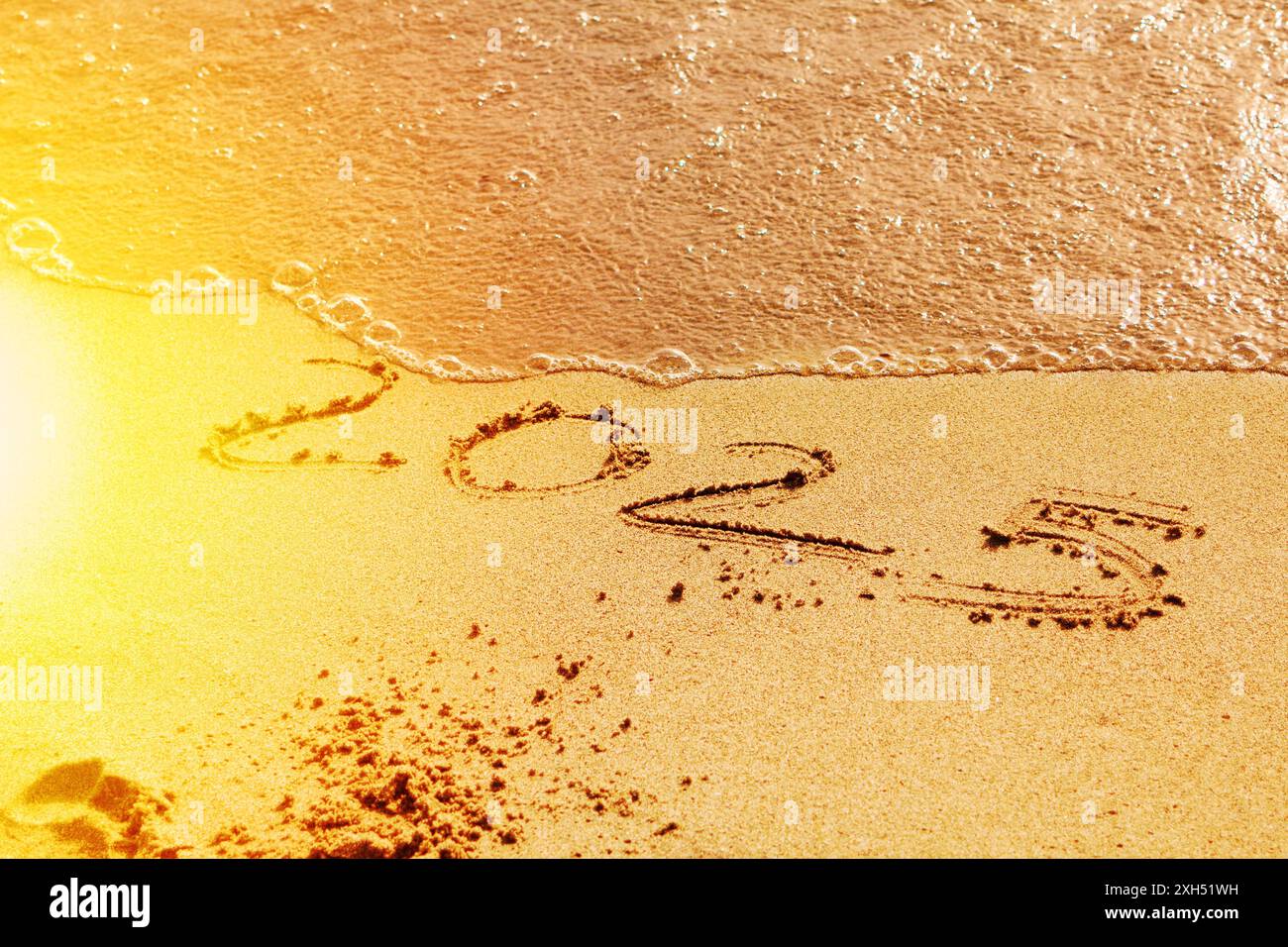 words "2025" and number written on the sand in the beach with waves ...