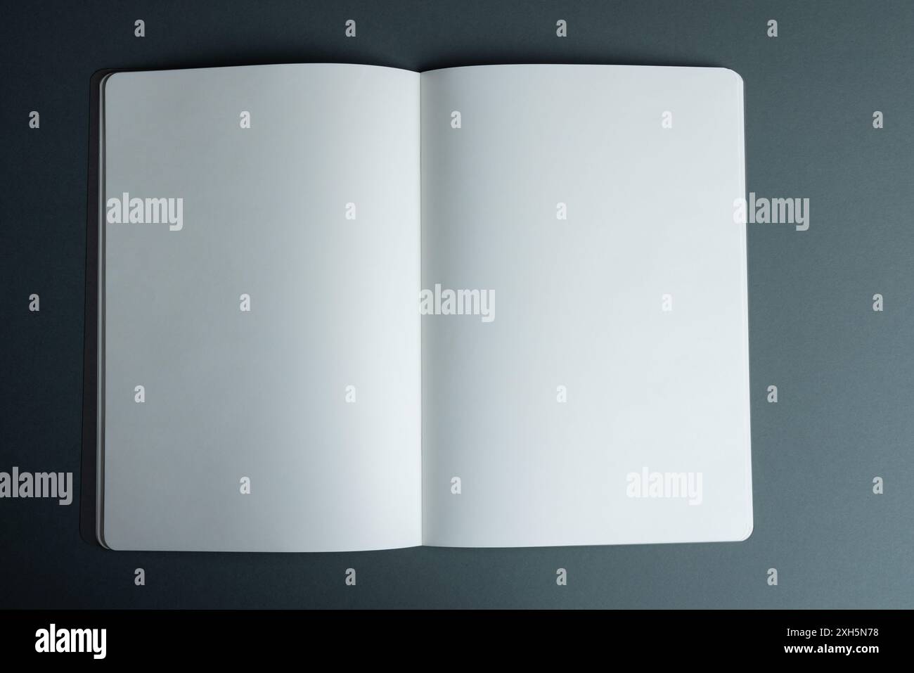 An open blank notebook lies on a dark surface, with copy space. Ideal for adding text or graphics, the notebook offers a clean slate for creativity or Stock Photo