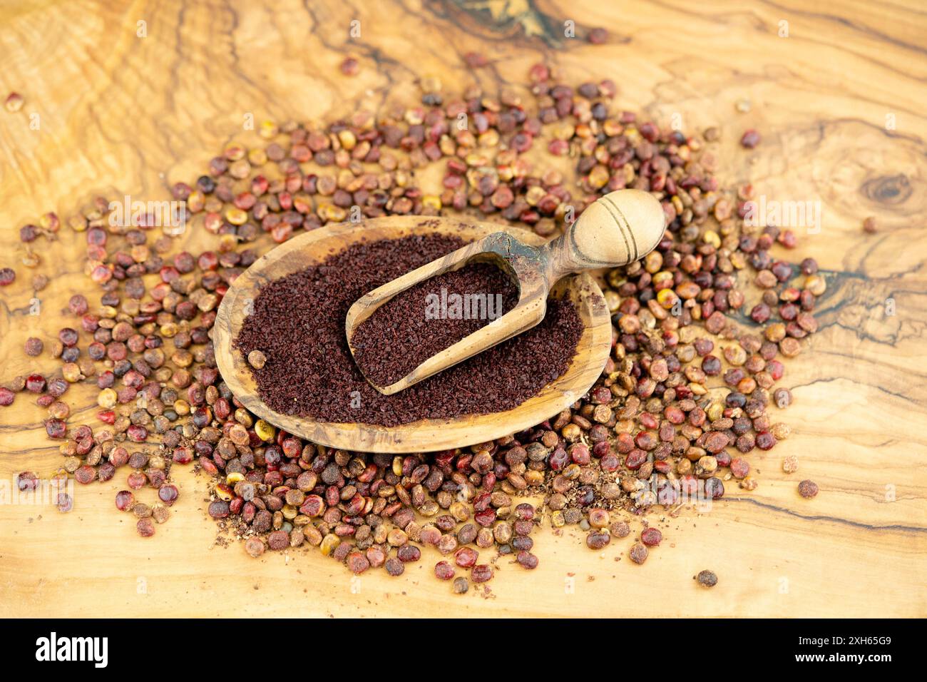 sicilian sumach (Rhus coriaria), dried sumac seeds, whole and ground on a wooden plate with a scoop Stock Photo