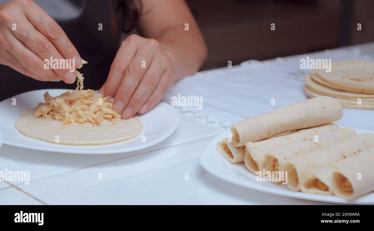 Woman chef preparing tacos in her kitchen, only her hands are seen rolling a tortilla to make delicious Mexican tacos, close-up view. Stock Photo