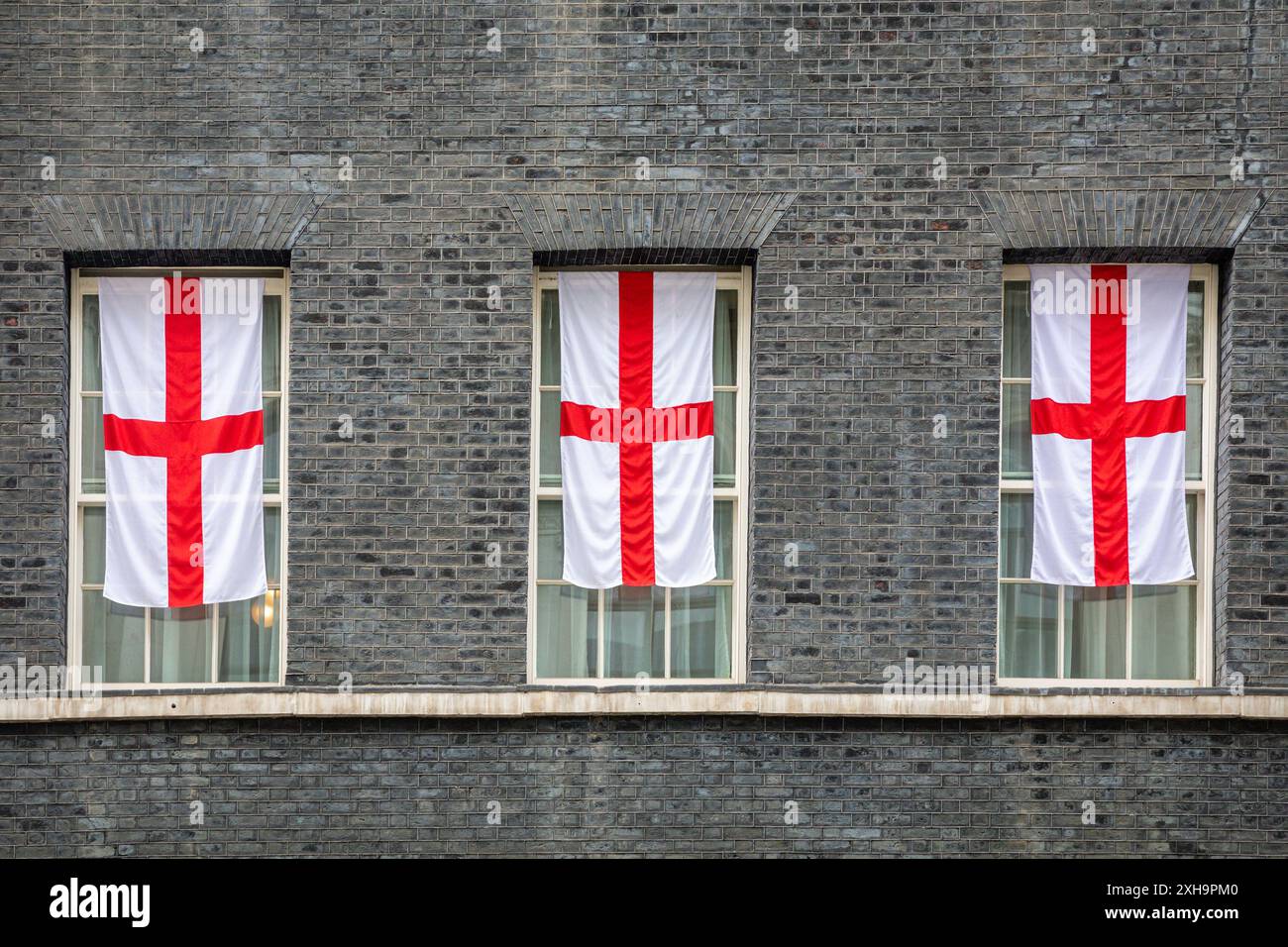 London, 12th July 2024. Three large St George's flags, the flag of England, were added to windows just above the No 10 Downing Street door, likely to symbolise the three lions (the common name for the England football team. The flags were added to the two rows of St George's cross bunting which were put up around the door and railings for the quarter final game. England play Spain in the final on Sunday. Credit: Imageplotter/Alamy Live News Stock Photo