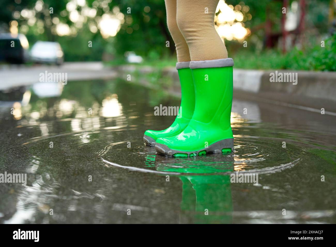 Little girl wearing green rubber boots standing in puddle outdoors ...