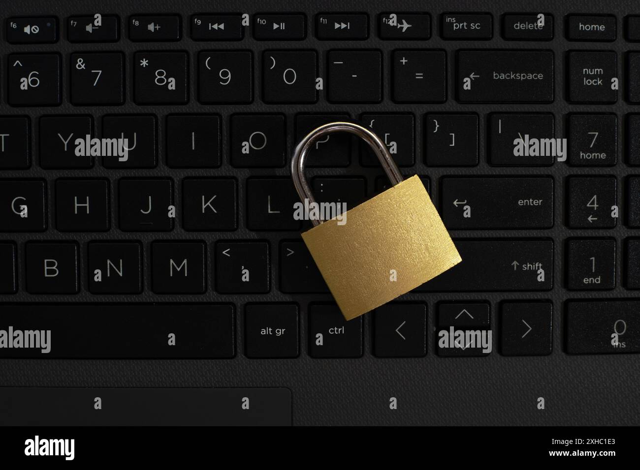 A gold padlock lies on a black laptop keyboard, with the padlock's hasp resting on the enter key. Stock Photo