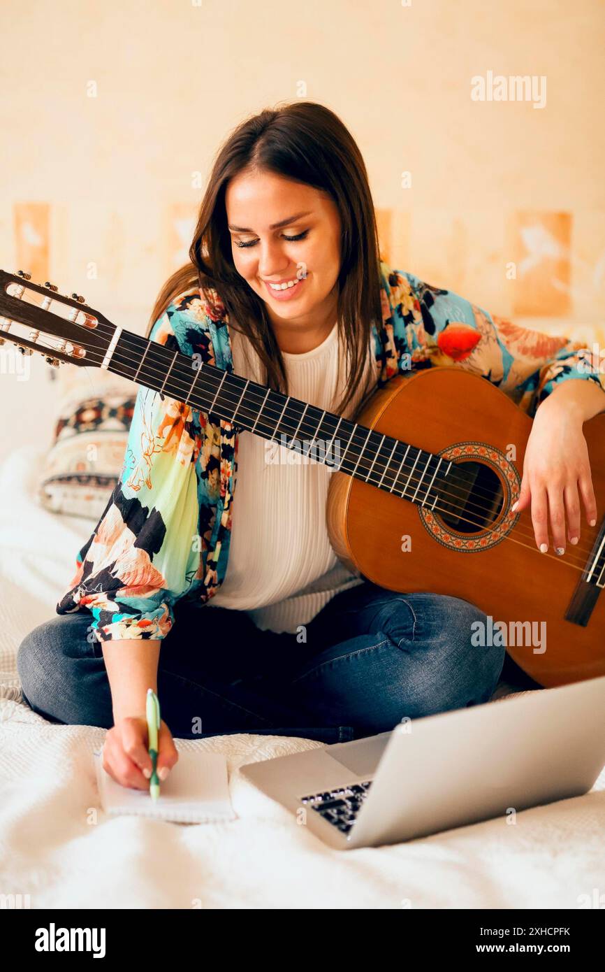 Singersb Using Note Crop female musician with acoustic guitar and laptop making notes while ...