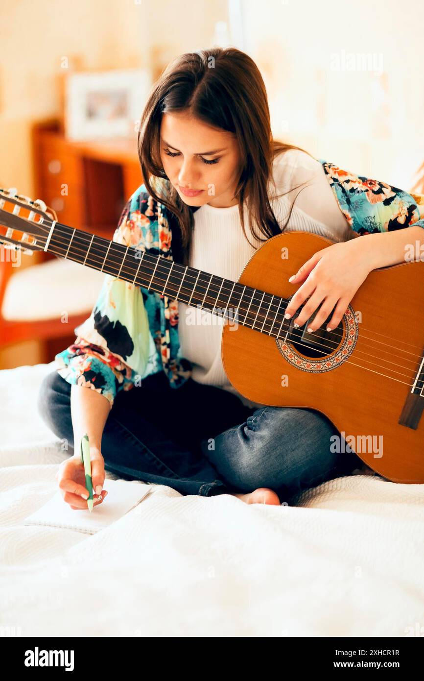 Singersb Using Note Crop female musician with acoustic guitar and laptop making notes while ...