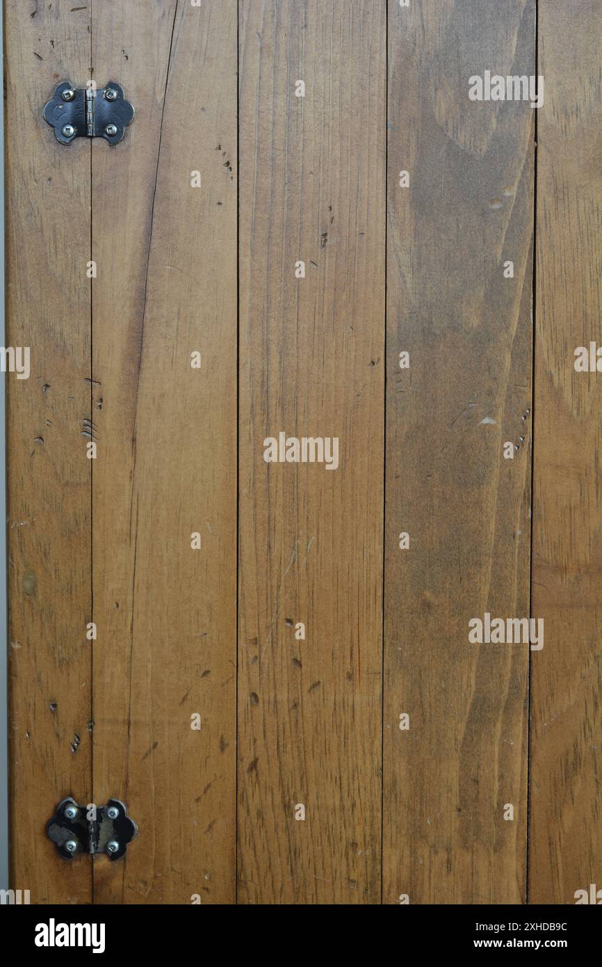 Close up of an old golden brown wooden cabinet showing the wood planks, wood grain, and black hardware hinges. Stock Photo