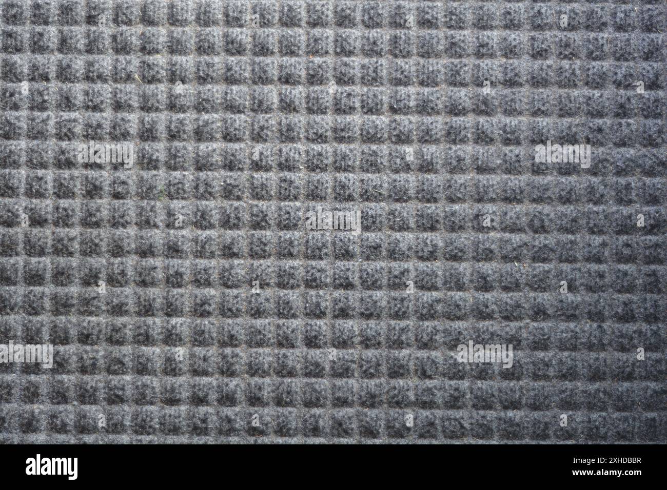 Close up of a gray door mat showing a symmetrical waffle pattern. Stock Photo