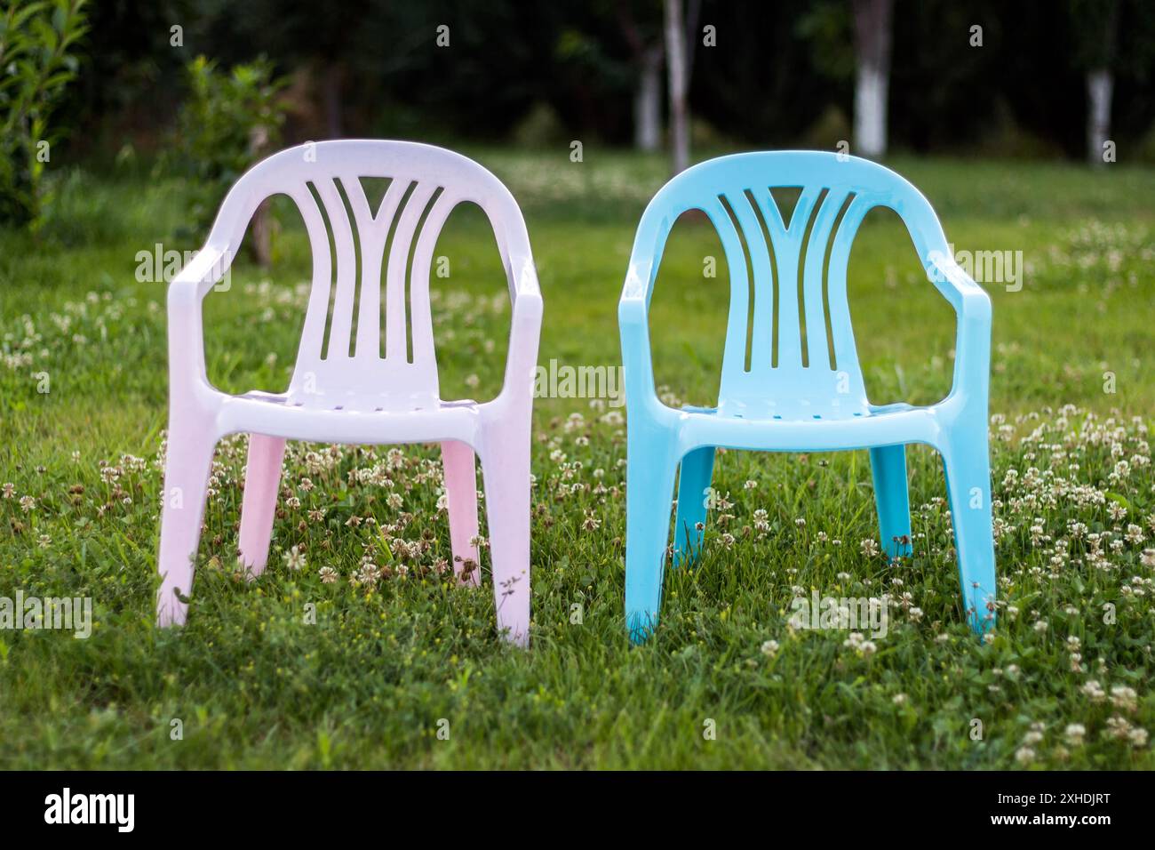Two plastic chairs, one pink and one blue, are positioned on a patch of green grass. Stock Photo