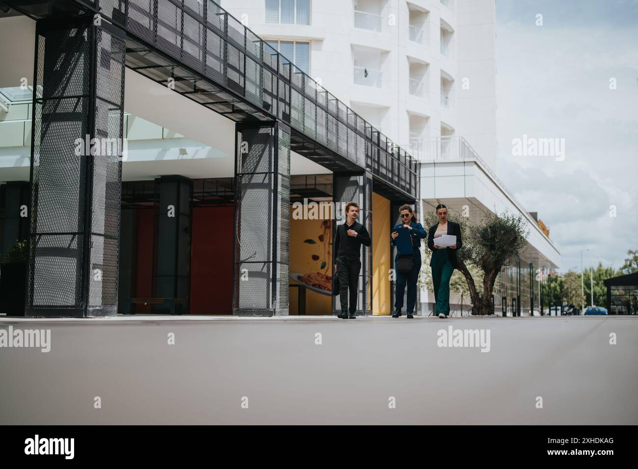 Three business professionals walking and discussing outside modern building Stock Photo