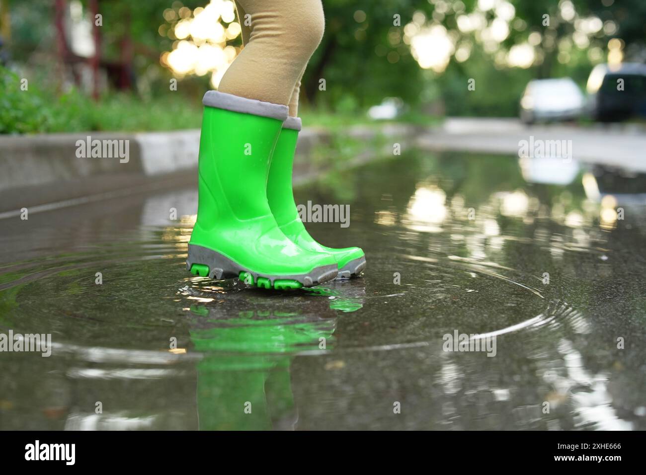 Little girl wearing green rubber boots standing in puddle outdoors ...