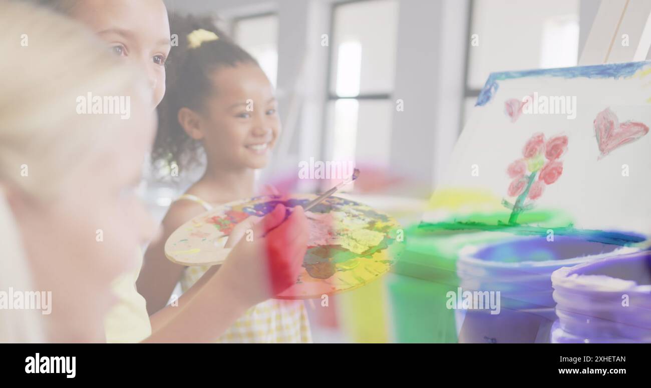 Image of paint pots over happy diverse schoolgirls painting in art class. Creativity, school, childhood, education and learning, digitally generated i Stock Photo