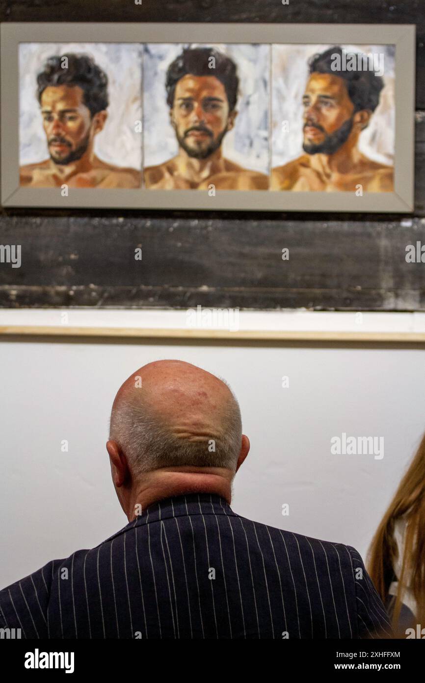 At a private view in small selling gallery in Rendham Suffolk an older man looks up a three portrait triptych of a dark haired bearded Caucasian man Stock Photo