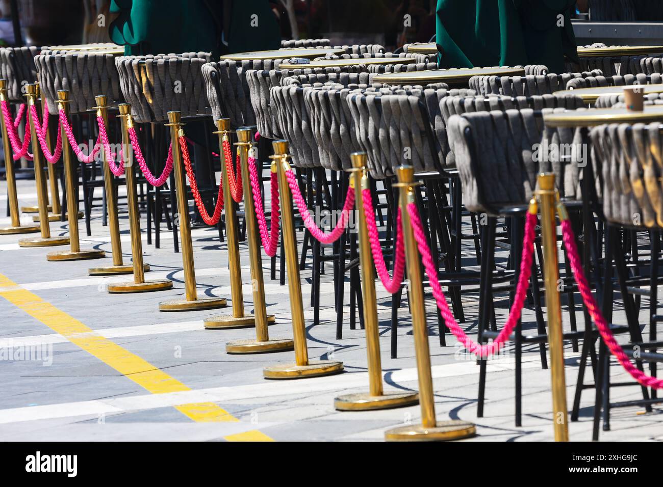 Row of chairs and poles with pink ropes tied to them, border of street restaurant Stock Photo