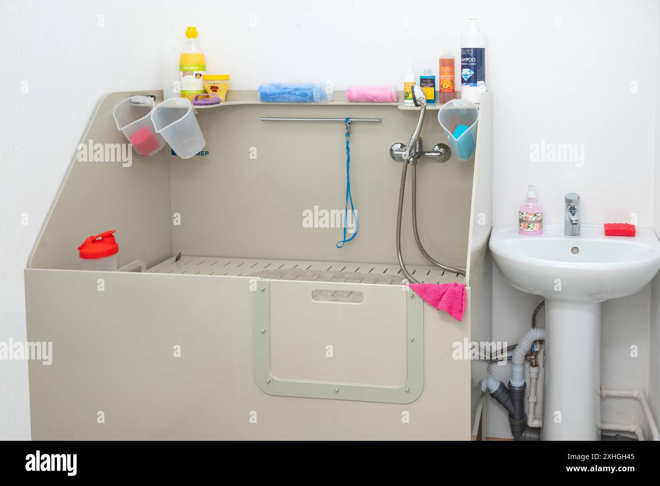 White plastic bathtub with non-slip mat, showerhead, sink, tiled walls, and window. Perfect for pet grooming, ensuring cleanliness and comfort in a pr Stock Photo