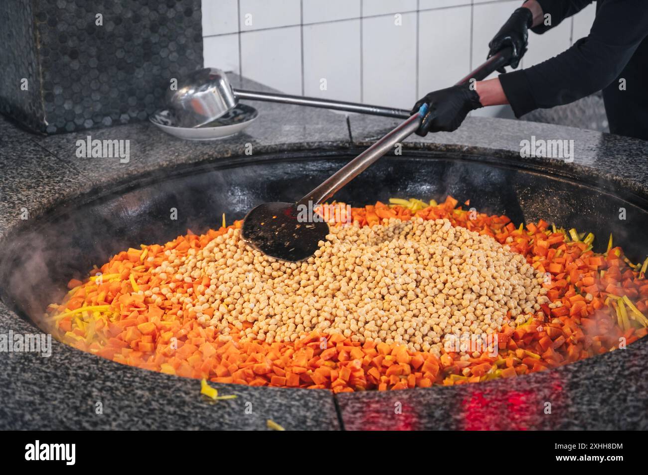 male cook stews carrots and chickpeas in a cauldron to cook traditional Uzbek pilaf in restaurant in Uzbekistan in Tashkent Stock Photo