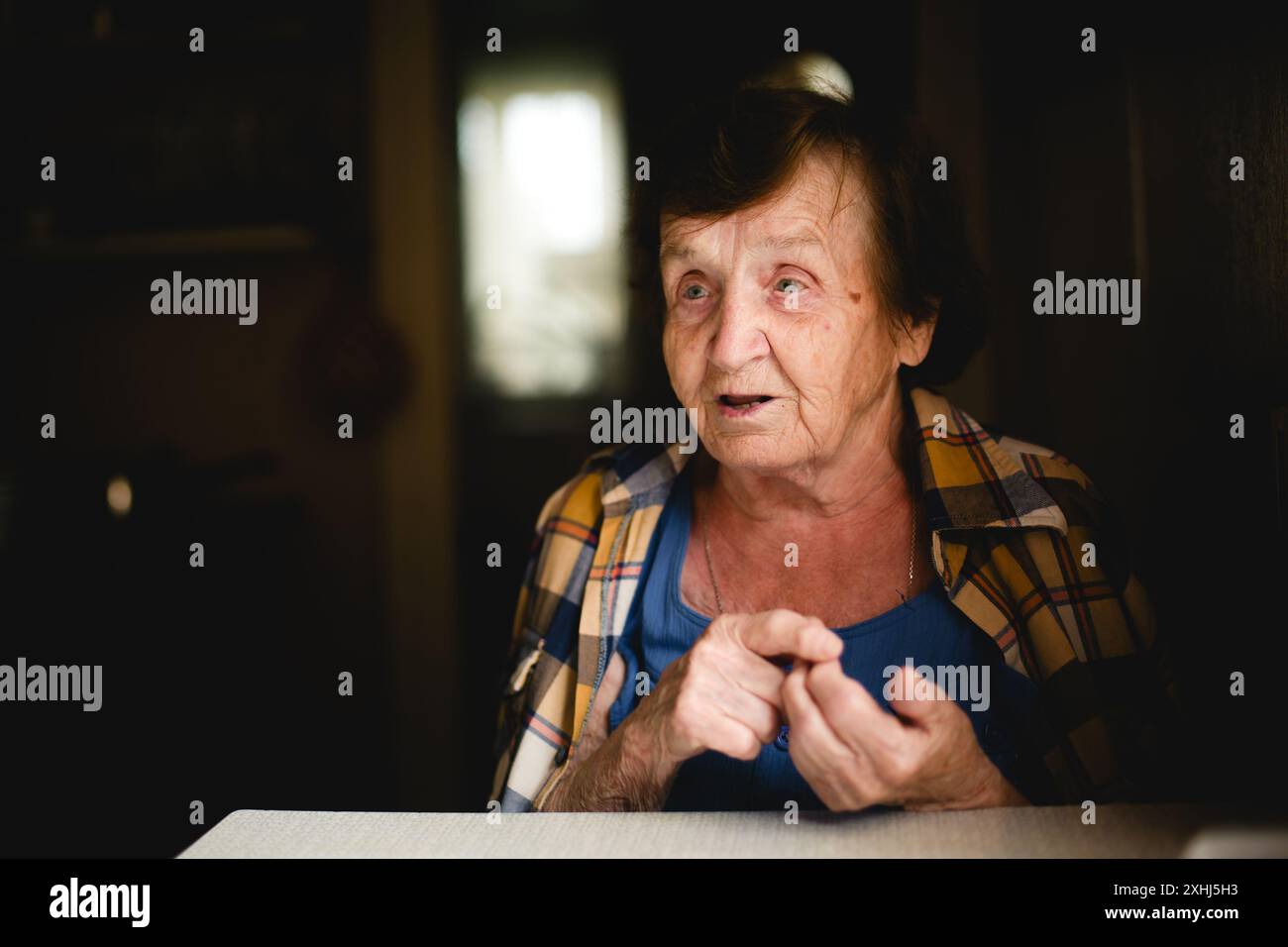 An elderly woman sits at the table, counting on her fingers as she tells a story. Stock Photo