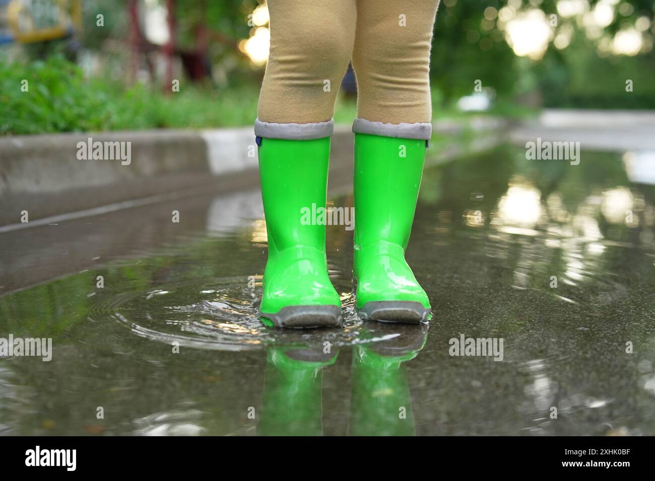 Little girl wearing green rubber boots standing in puddle outdoors ...