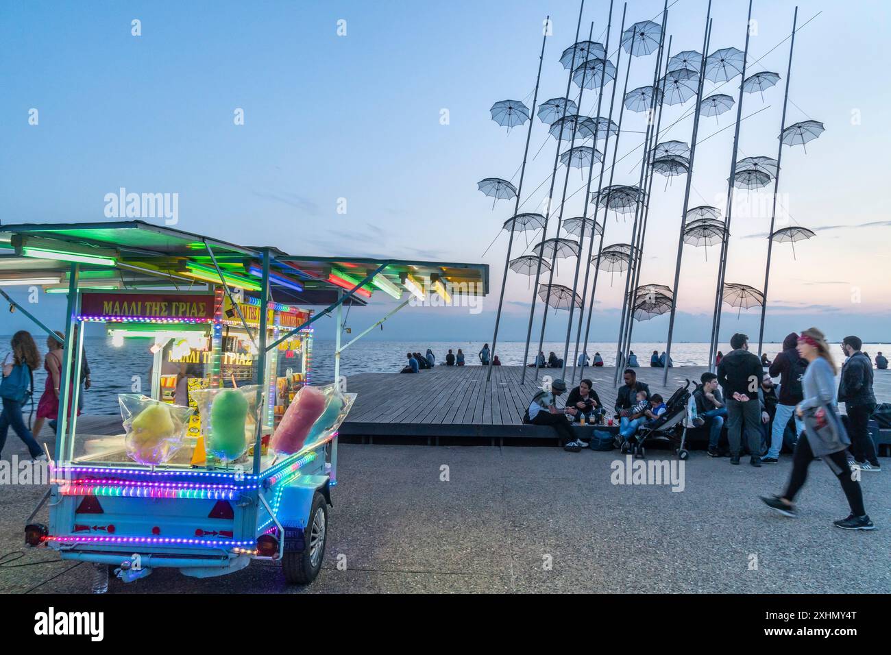 People relaxing and watching the sunset by The umbrellas sculpture on Thessaloniki waterfront, Macedonia, Northern Greece Stock Photo