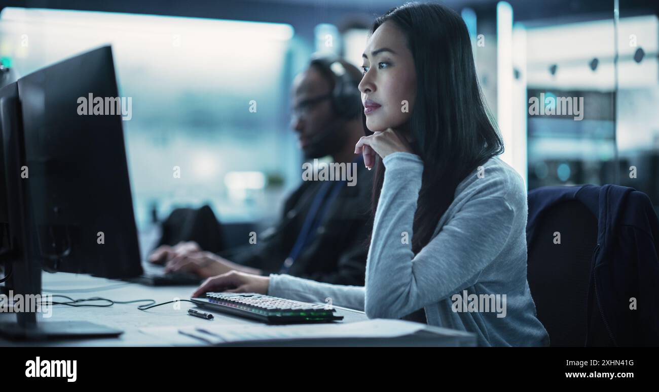 Beautiful Young Asian Female Specialist Working on Computer Together with Professional Colleagues. Data Protection Center with Server Facility, Storage Hardware and Corporate Science Atmosphere Stock Photo