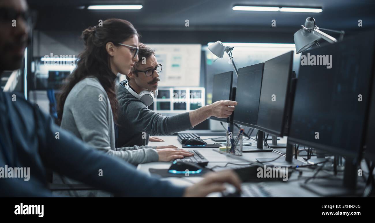 Young Colleagues Working on Computers and Talking at a Workplace. Female and Male Software Developers Discussing a Solution for Their Collaborative Artificial Intelligence Project Stock Photo
