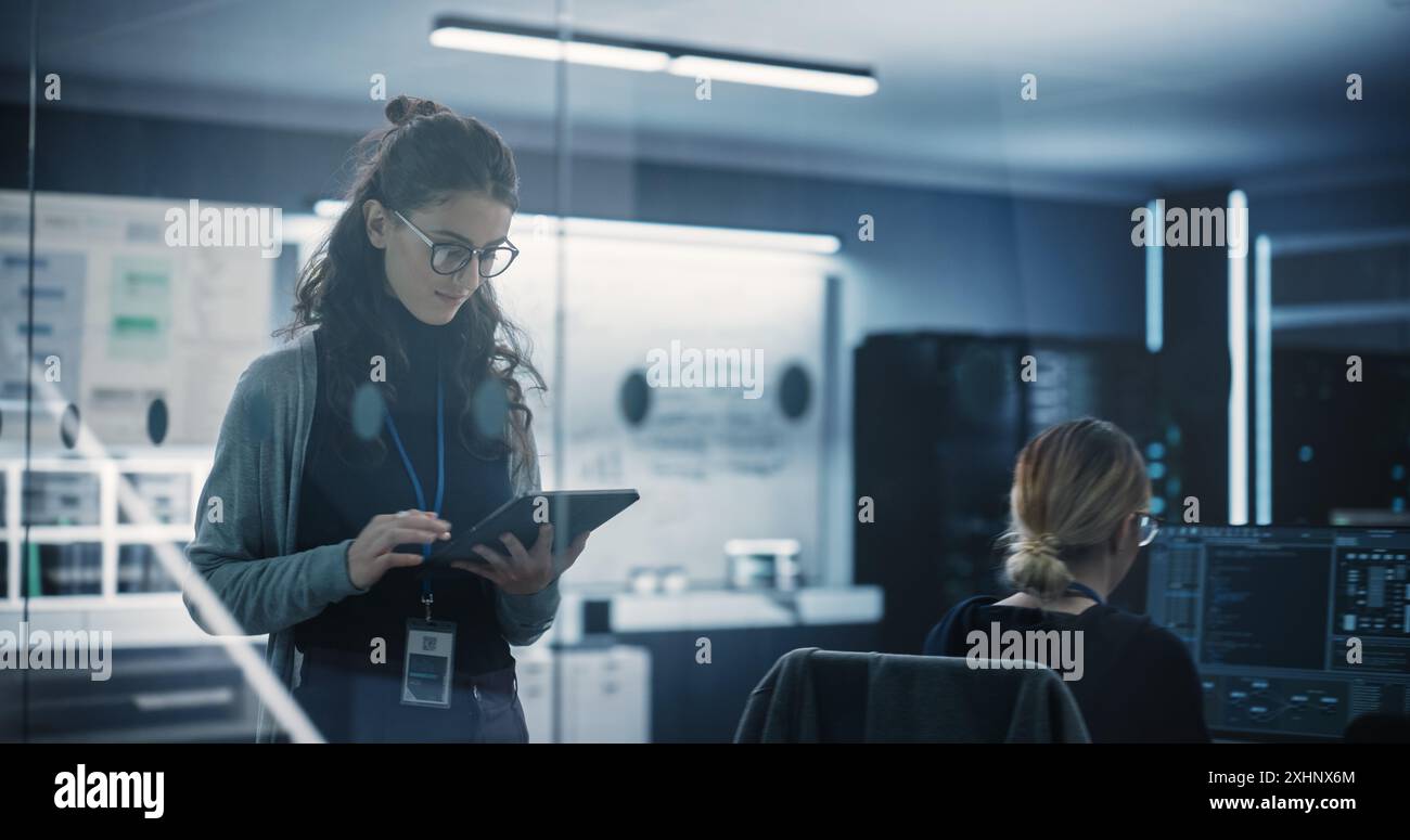 Technological Software Engineering Department Manager Walking and Using a Tablet Computer. Multiethnic Female Working in the Office Stock Photo