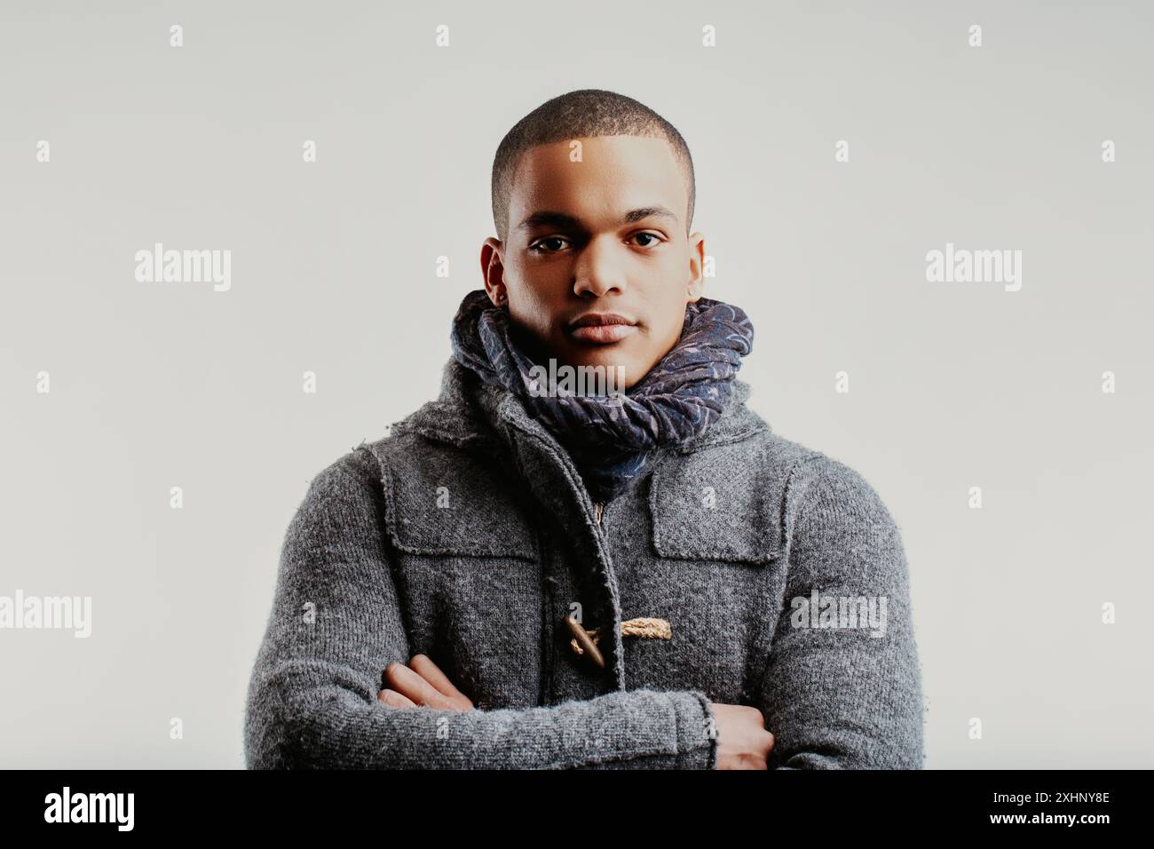 Man in a grey coat and blue scarf, arms crossed, exuding confidence and seriousness. His neatly trimmed hair and direct gaze convey a sense of strengt Stock Photo
