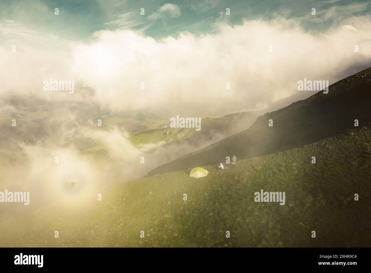 Aerial scenic morning view couple stand camping enjoy sunshine by tent. Circular halo in nature outdoors while camping in misty mountains. Hidden gem Stock Photo