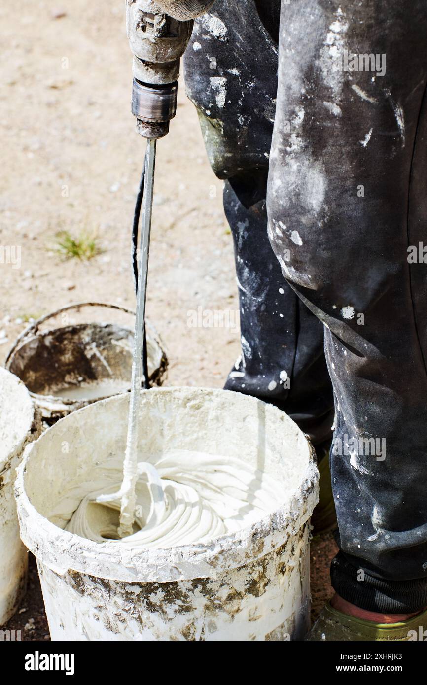 Paddle mixer for cement adhesive mortar connects to electric drill for decorating and building jobs, construction worker mixes tile glue mortar in buc Stock Photo