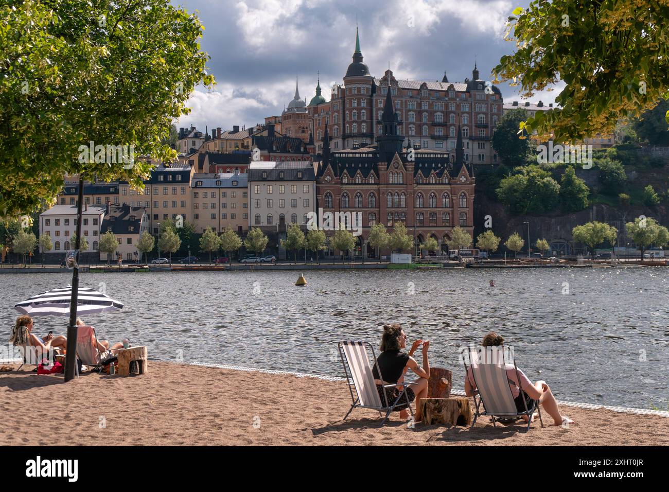 People enjoying the summer sun infront of historical buildings of Södermalm, from the island of Riddarholmen, near Lake Mälaren, Stockholm, Sweden Stock Photo