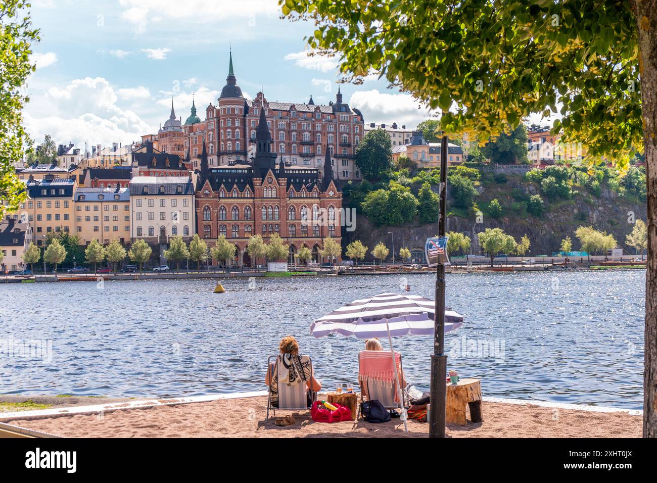 People enjoying the summer sun infront of historical buildings of Södermalm, from the island of Riddarholmen, near Lake Mälaren, Stockholm, Sweden Stock Photo
