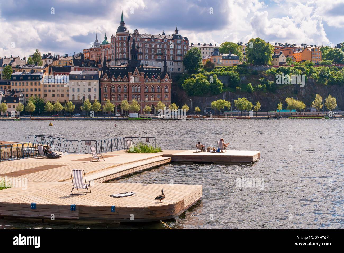 People enjoying the summer sun infront of historical buildings of Södermalm, from the island of Riddarholmen, near Lake Mälaren, Stockholm, Sweden Stock Photo