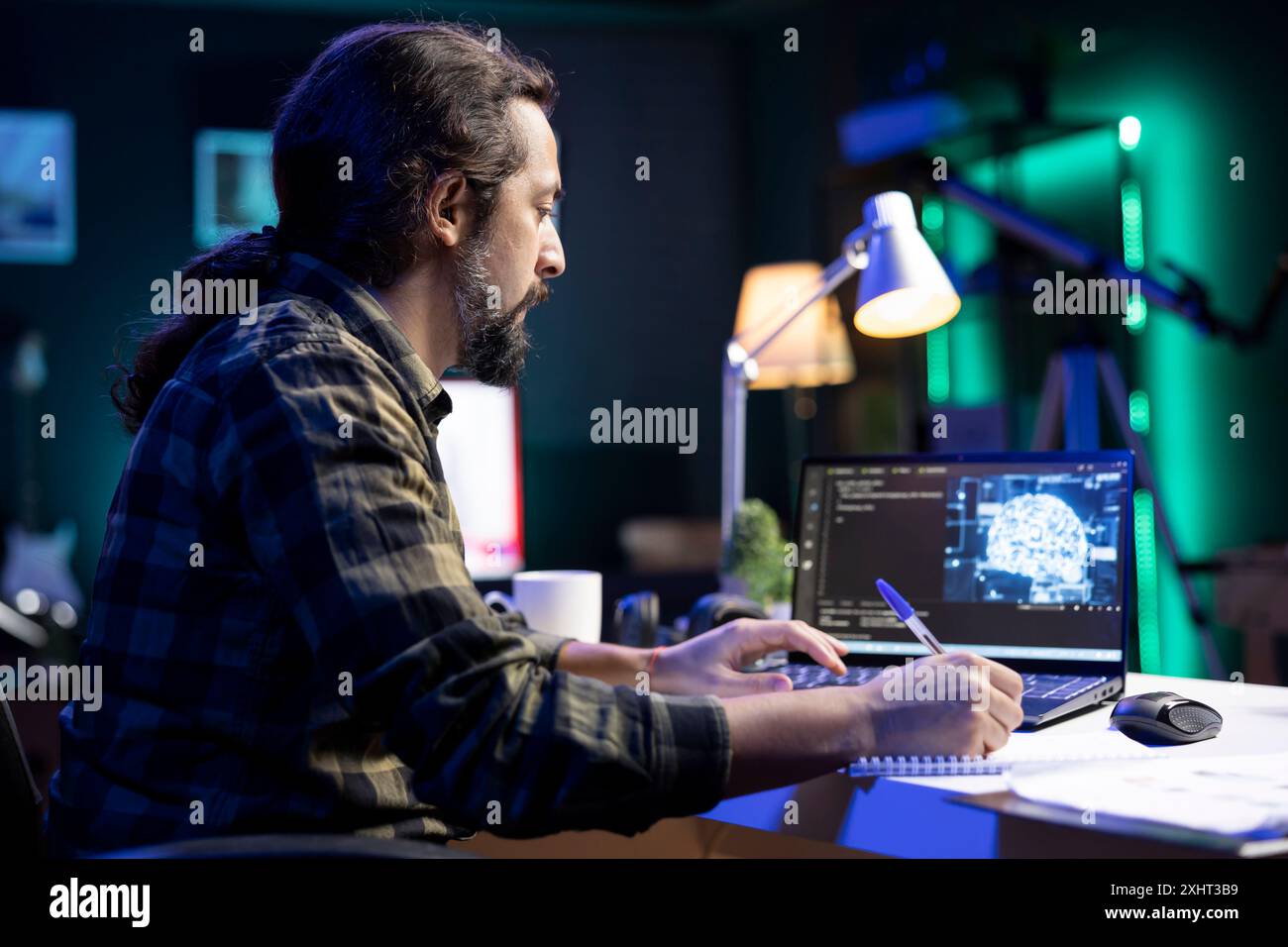Man at desk using laptop for programming and data analysis. Male programmer working at home, using his notepad while efficiently managing information technology and data center on digital device. Stock Photo