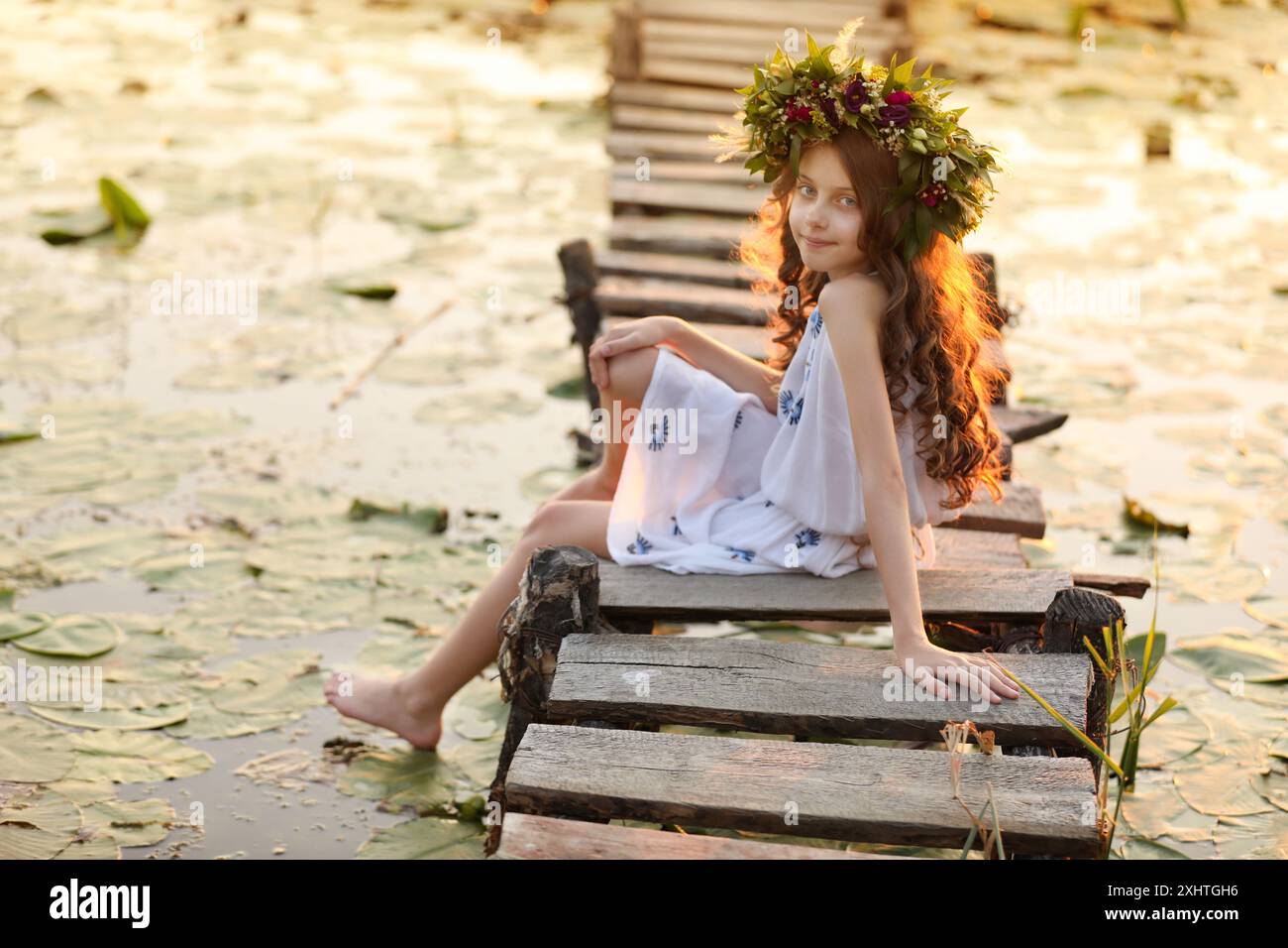 Cute little girl wearing wreath made of beautiful flowers on pier near ...