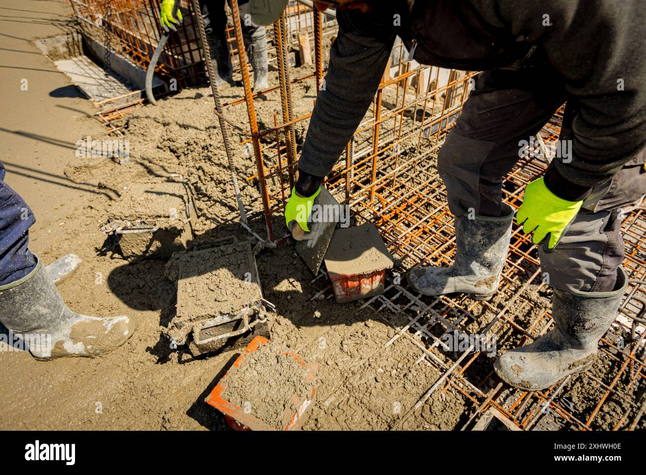 Worker is using trowel to fill up cube mold, full with concrete, sample ...