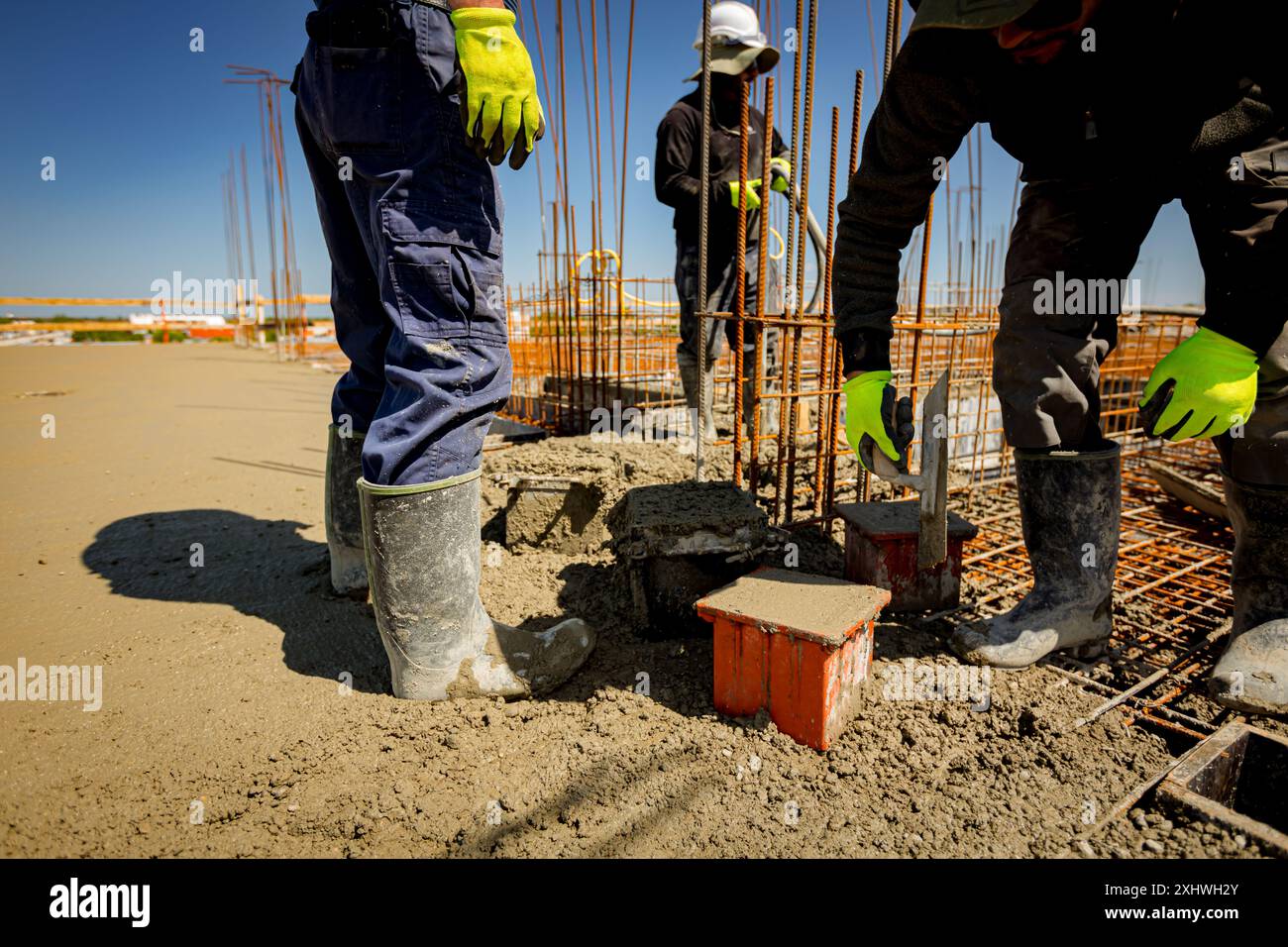 Worker is using trowel to fill up cube mold, full with concrete, sample ...